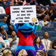 Charlotte Hornets mascot "Hugo" holds up signs to a fan.